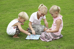 Parents can work from home with kids playing board games like these three blond-haired children are doing.