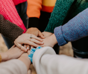 Social media for authors can help build a community, represented by this group of people standing in a circle huddle with their hands in the middle.