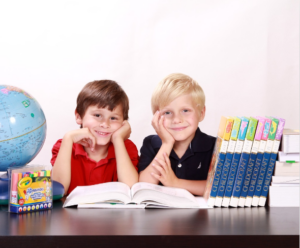 Social media for authors, when done right, contributes to learning, depicted by these two boys sitting at a desk with a computer, encyclopedias, a globe, and art supplies.